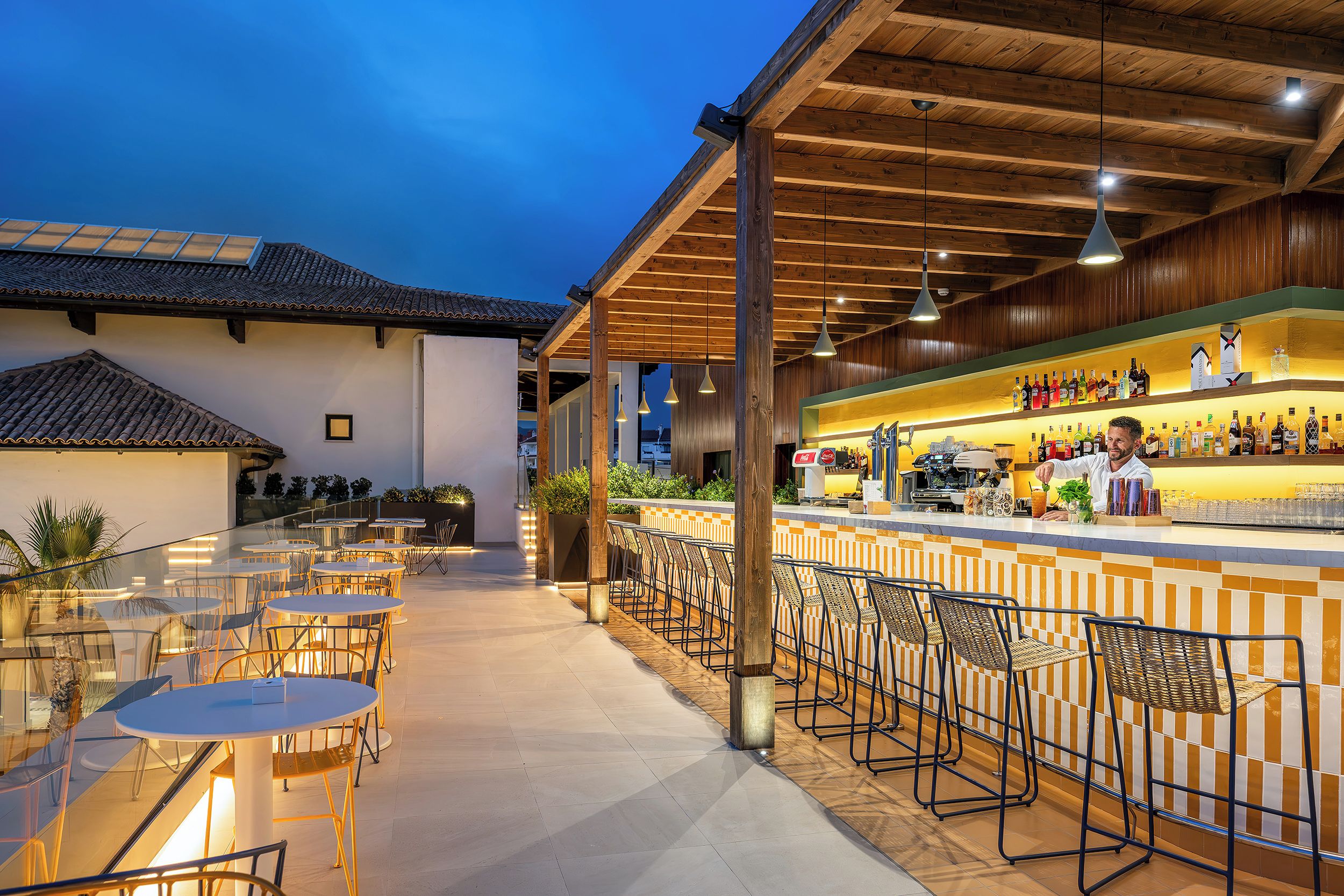 An outdoor bar area with a long counter, bar stools, and tables.