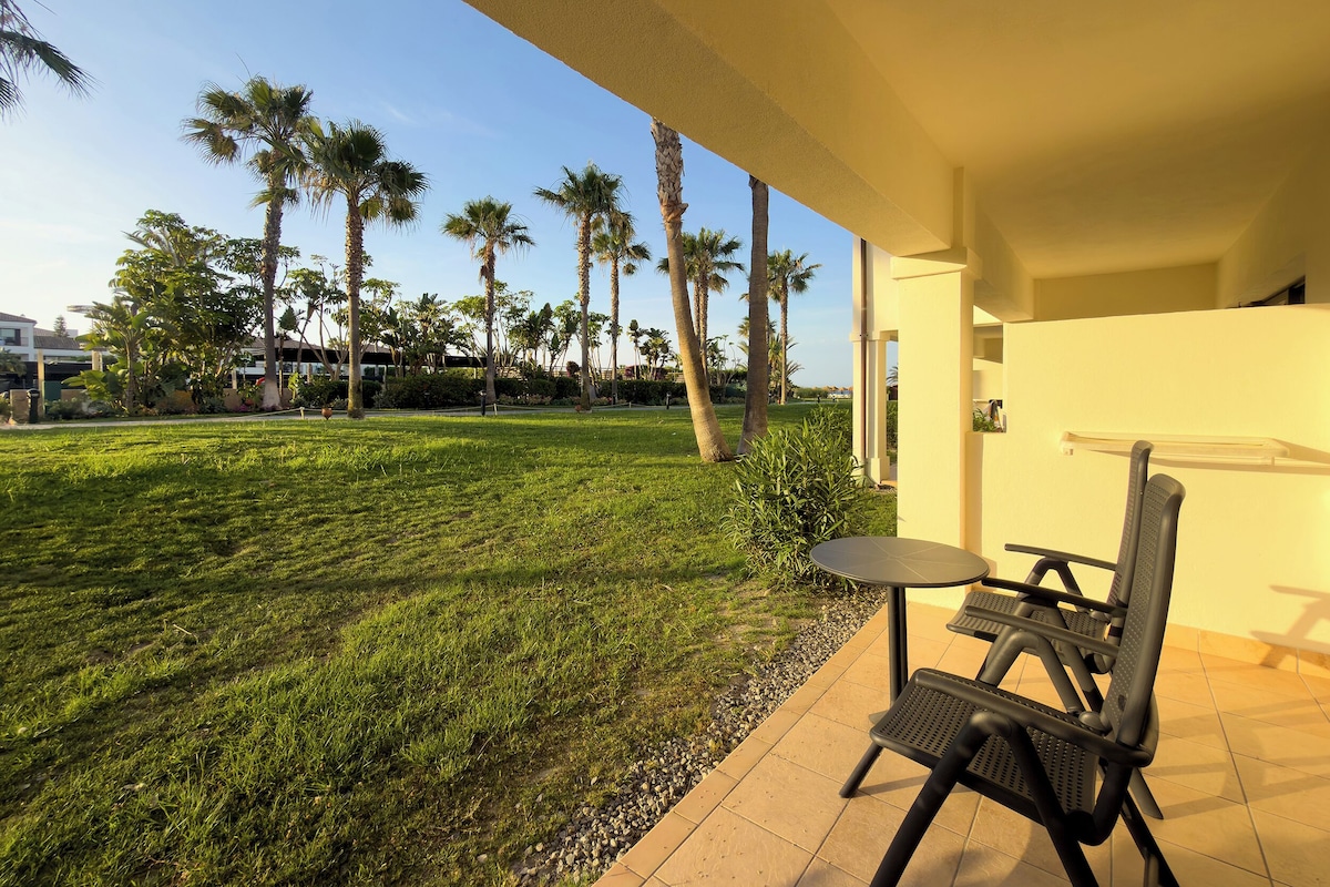 A patio area with a table and chairs, surrounded by a well-maintained lawn and palm trees.