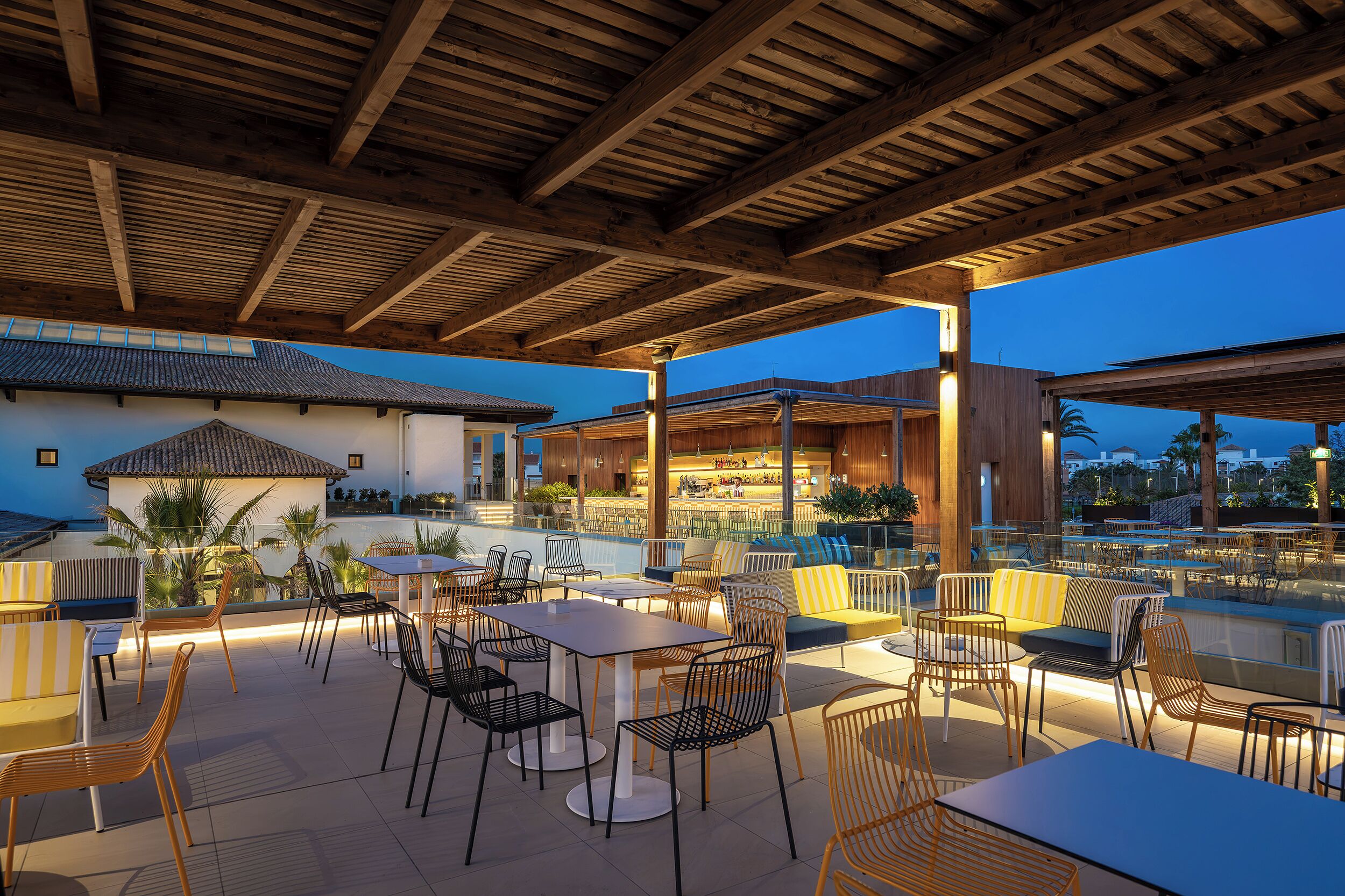 An outdoor patio area with tables and chairs, a pool, and a bar area.