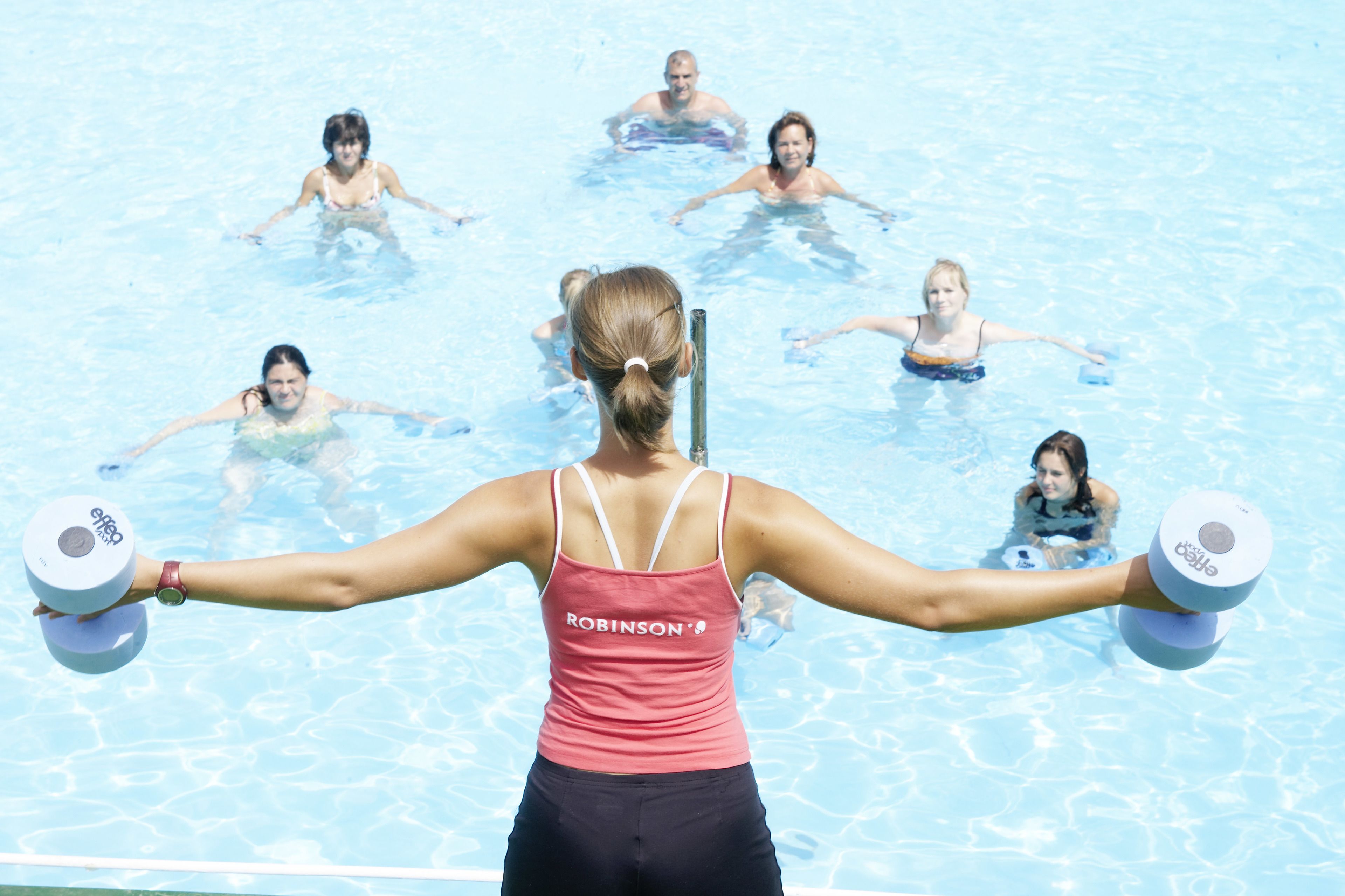 Piscina con persone che nuotano e una persona in primo piano che solleva pesi.