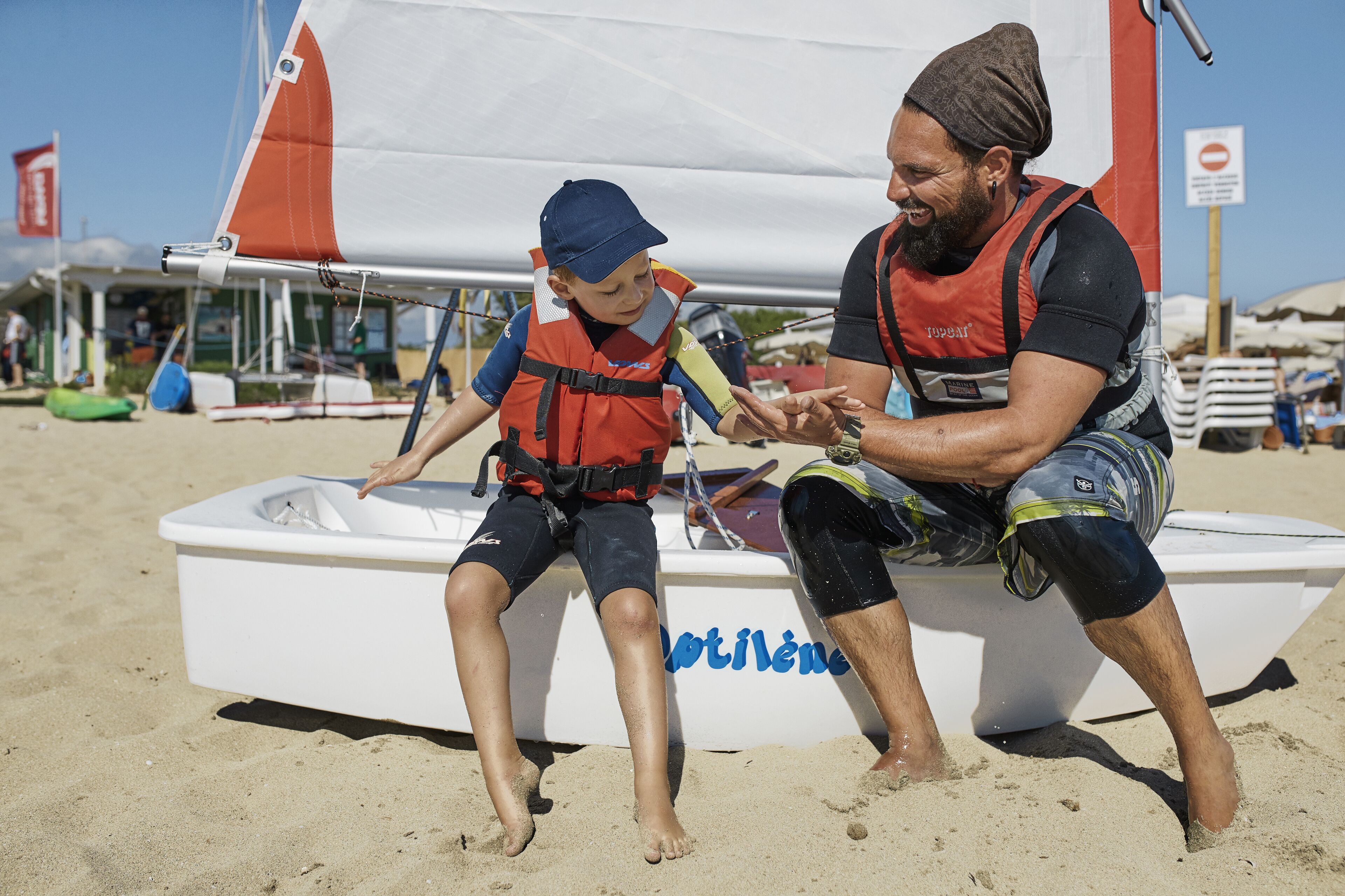Ein Mann und ein Kind sitzen auf dem Sand, während sie auf einem Boot namens "MOTILENE" sitzen.