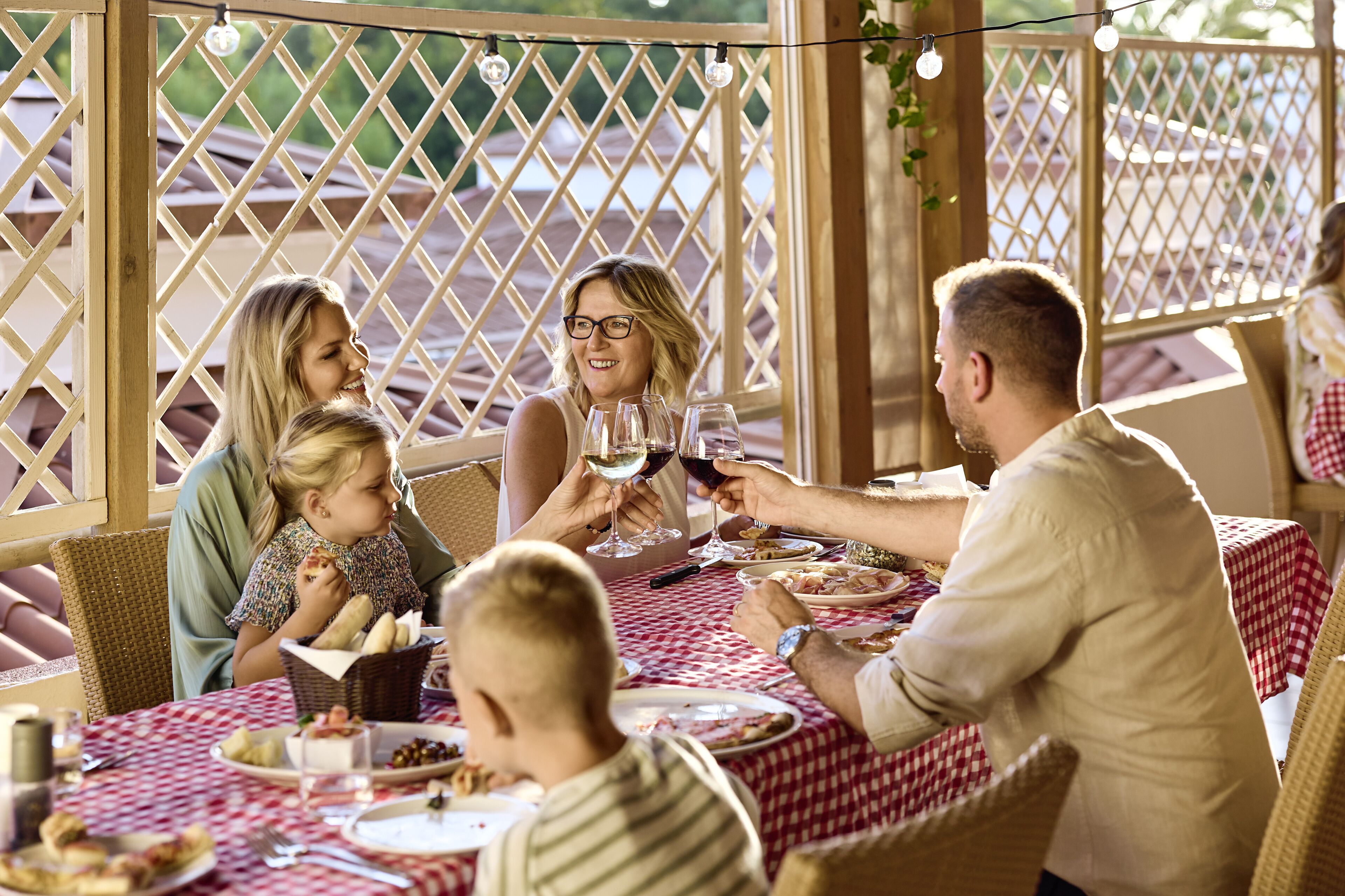 Una familia cenando en una mesa al aire libre con un fondo de celosía y luces colgantes.