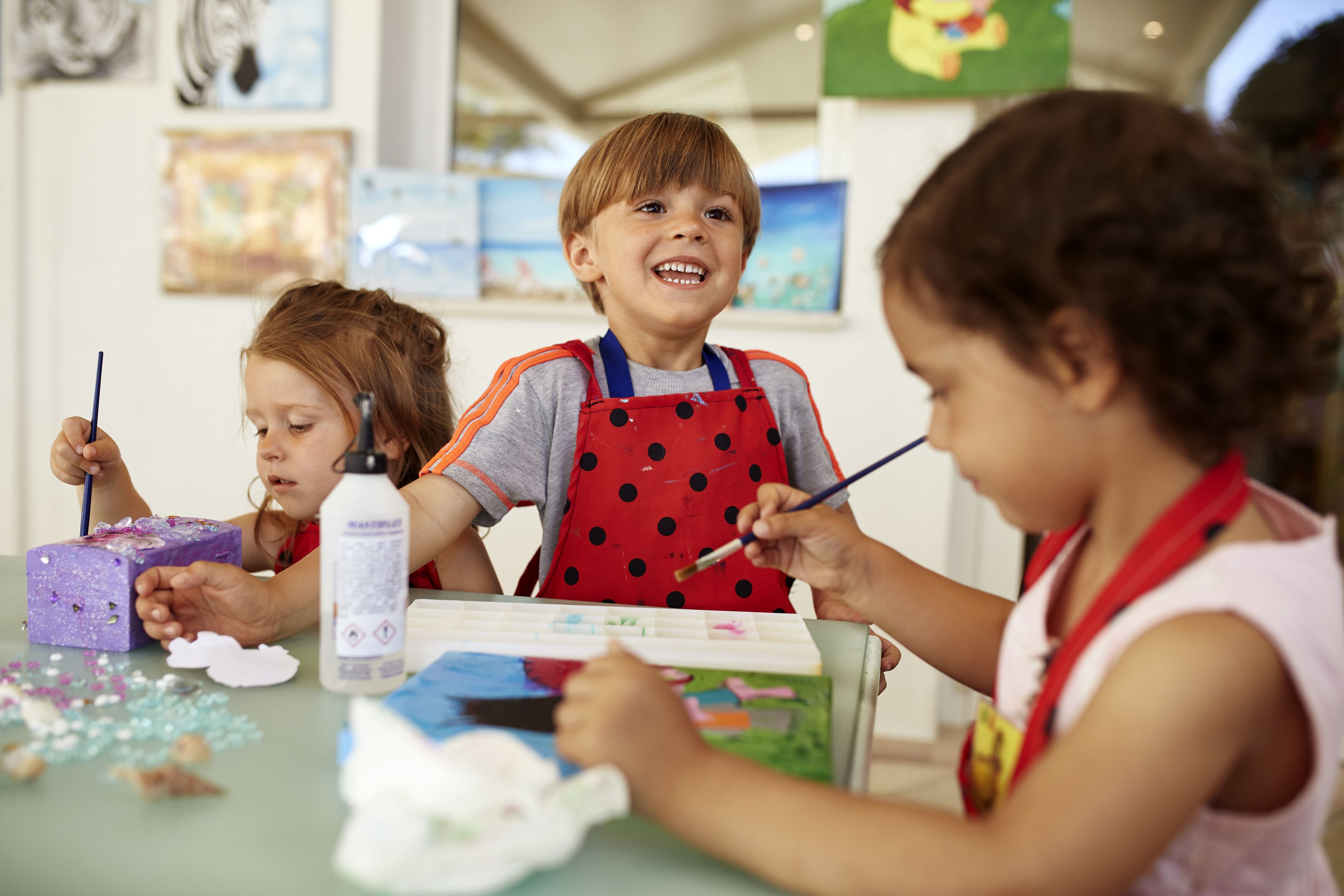Niños pintando en una mesa con materiales de arte.