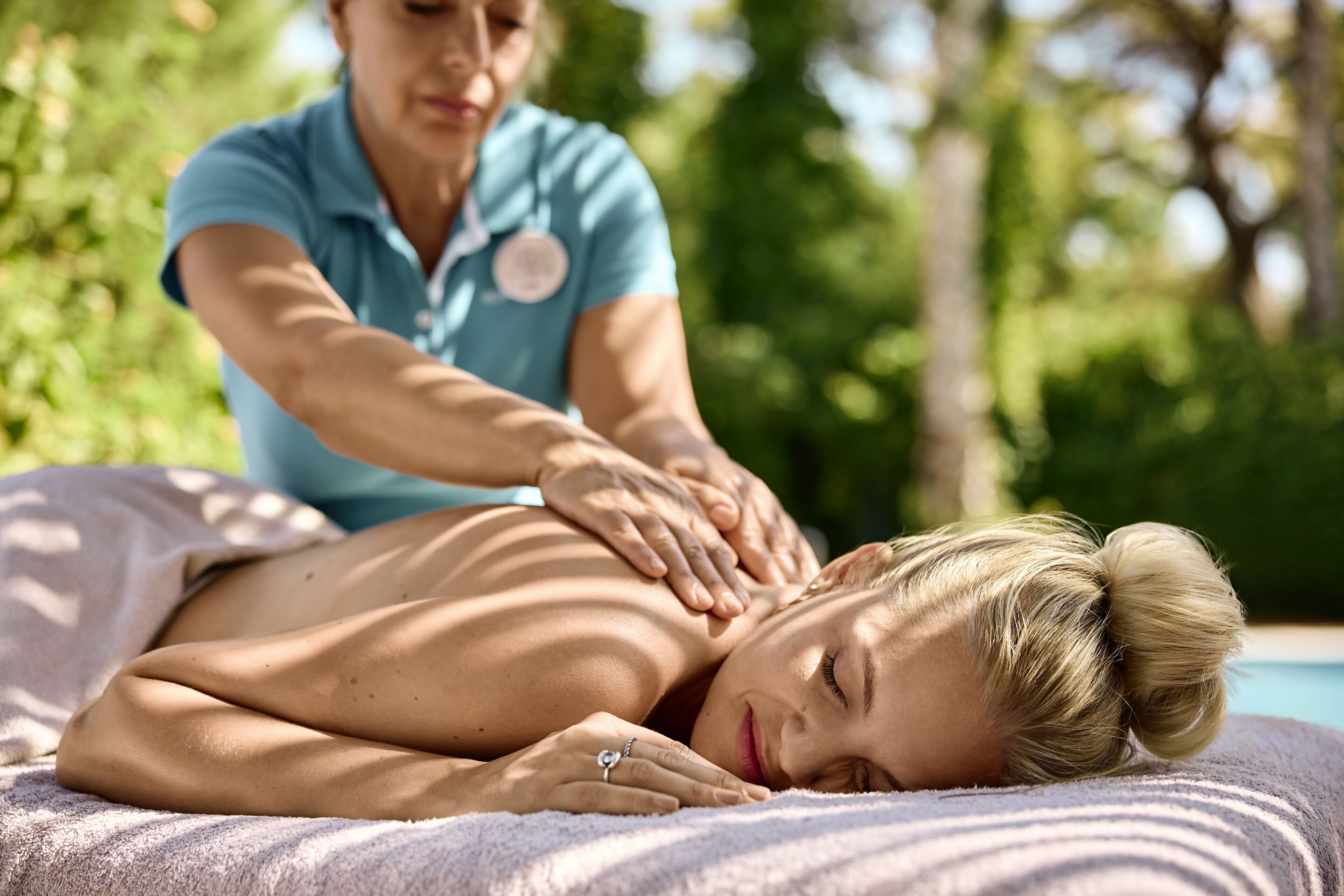 A person receiving a massage outdoors with a pool in the background.