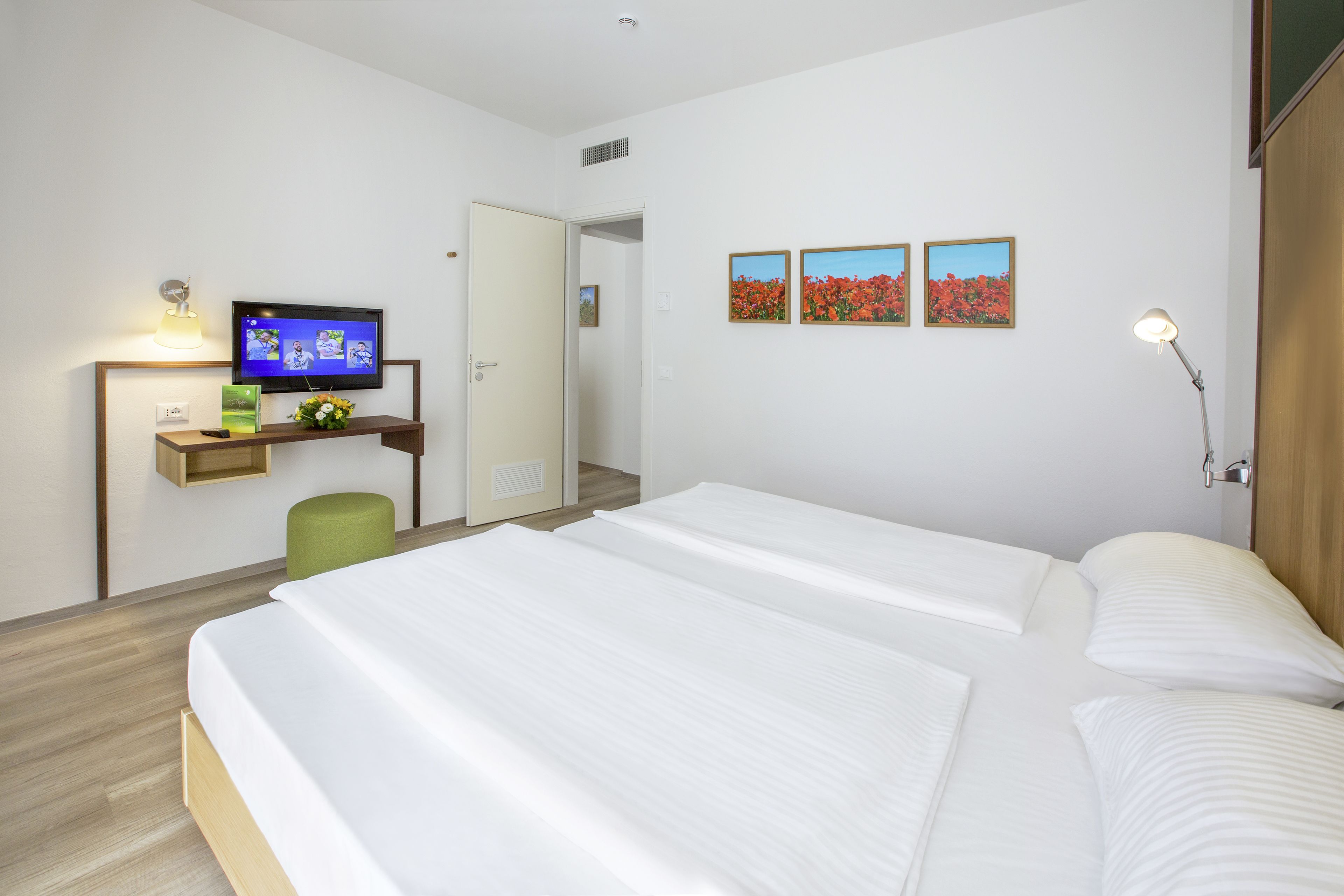 A hotel room with two beds, a desk with a television, and three framed pictures on the wall.