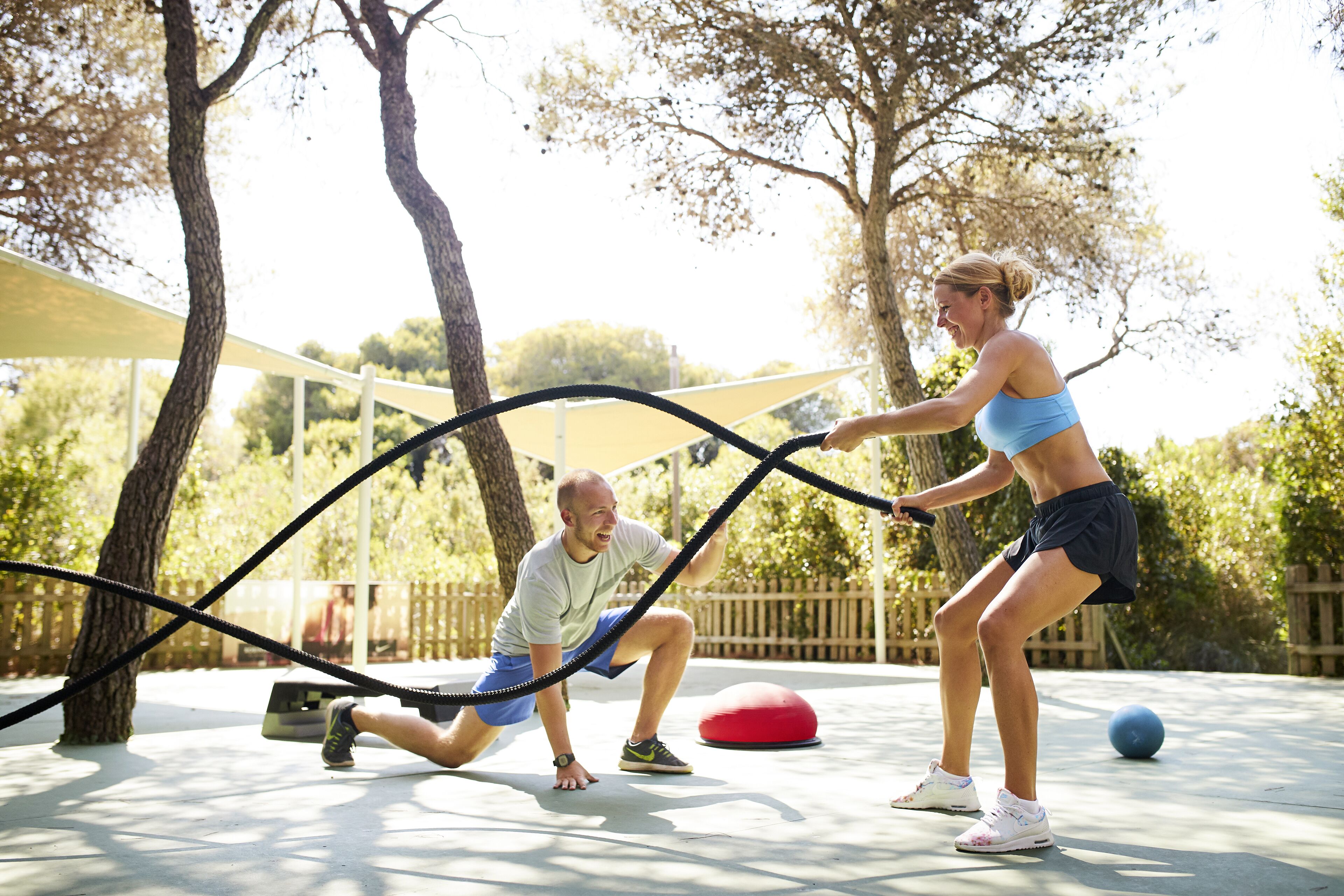 An outdoor exercise area with ropes, a red exercise ball, and trees.