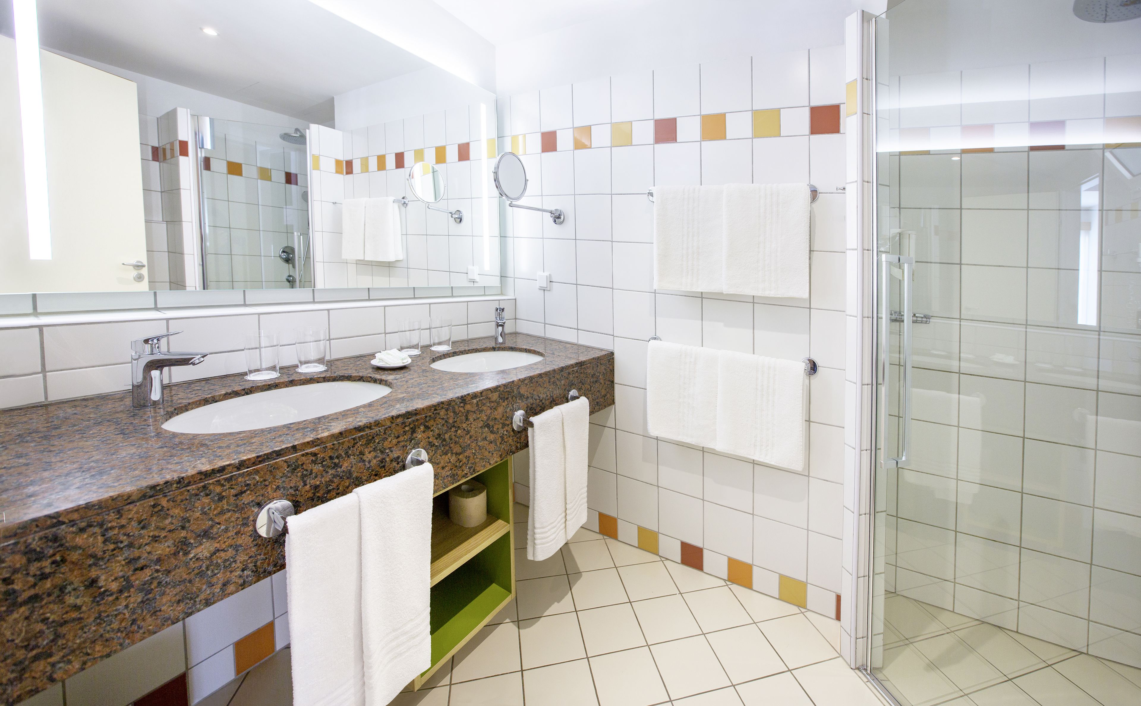 A modern bathroom with two sinks, a glass shower enclosure, and a large mirror.
