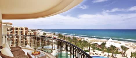 A balcony with wicker furniture, a pool, and a beach view.