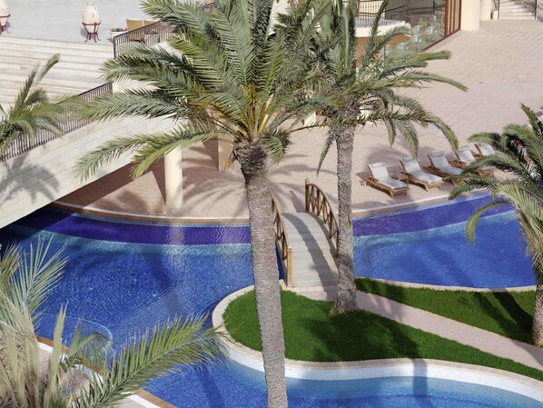 A pool area with palm trees, lounge chairs, and a bridge. - Mövenpick Resort & Marine Spa Sousse (Sousse)