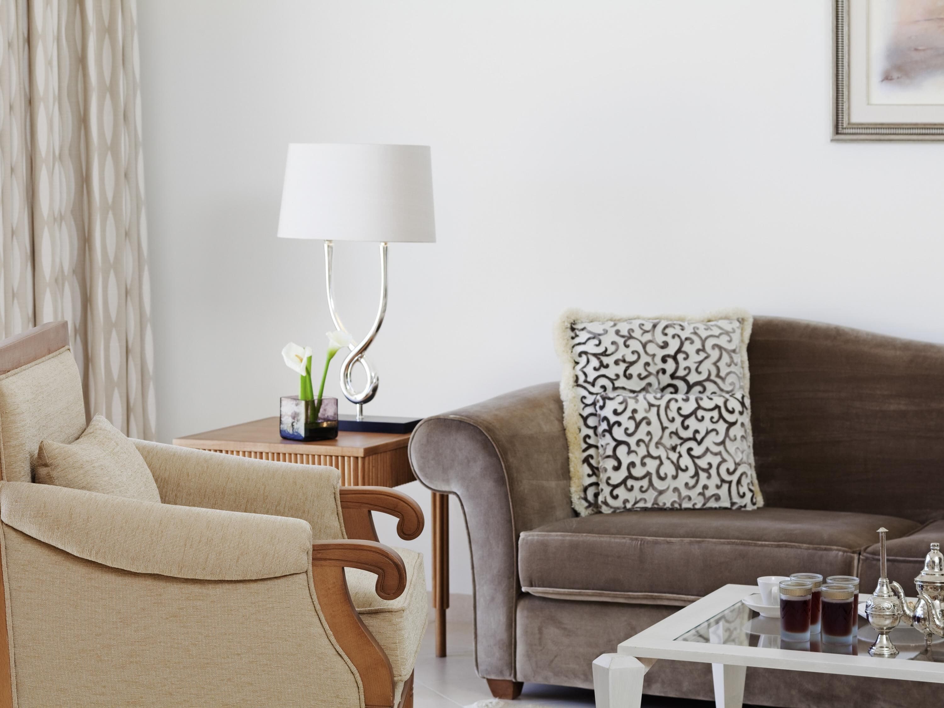 A living room with a sofa, armchair, table, lamp, and decorative items.