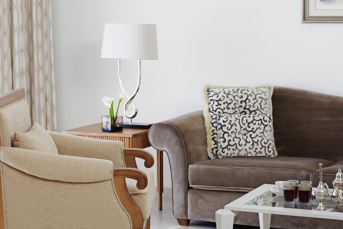 A living room with a sofa, armchair, table, lamp, and decorative items.