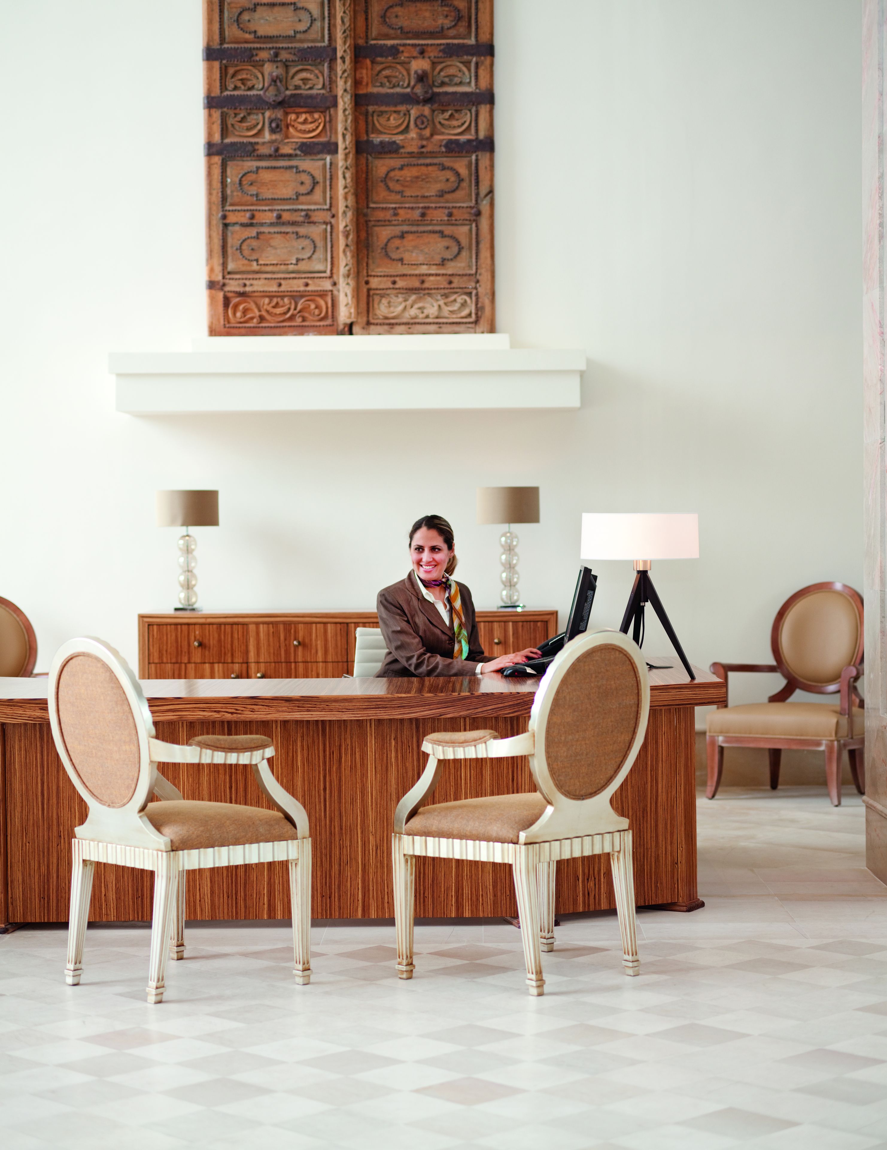 A reception desk with two chairs, a wooden panel wall, and a large mirror above.