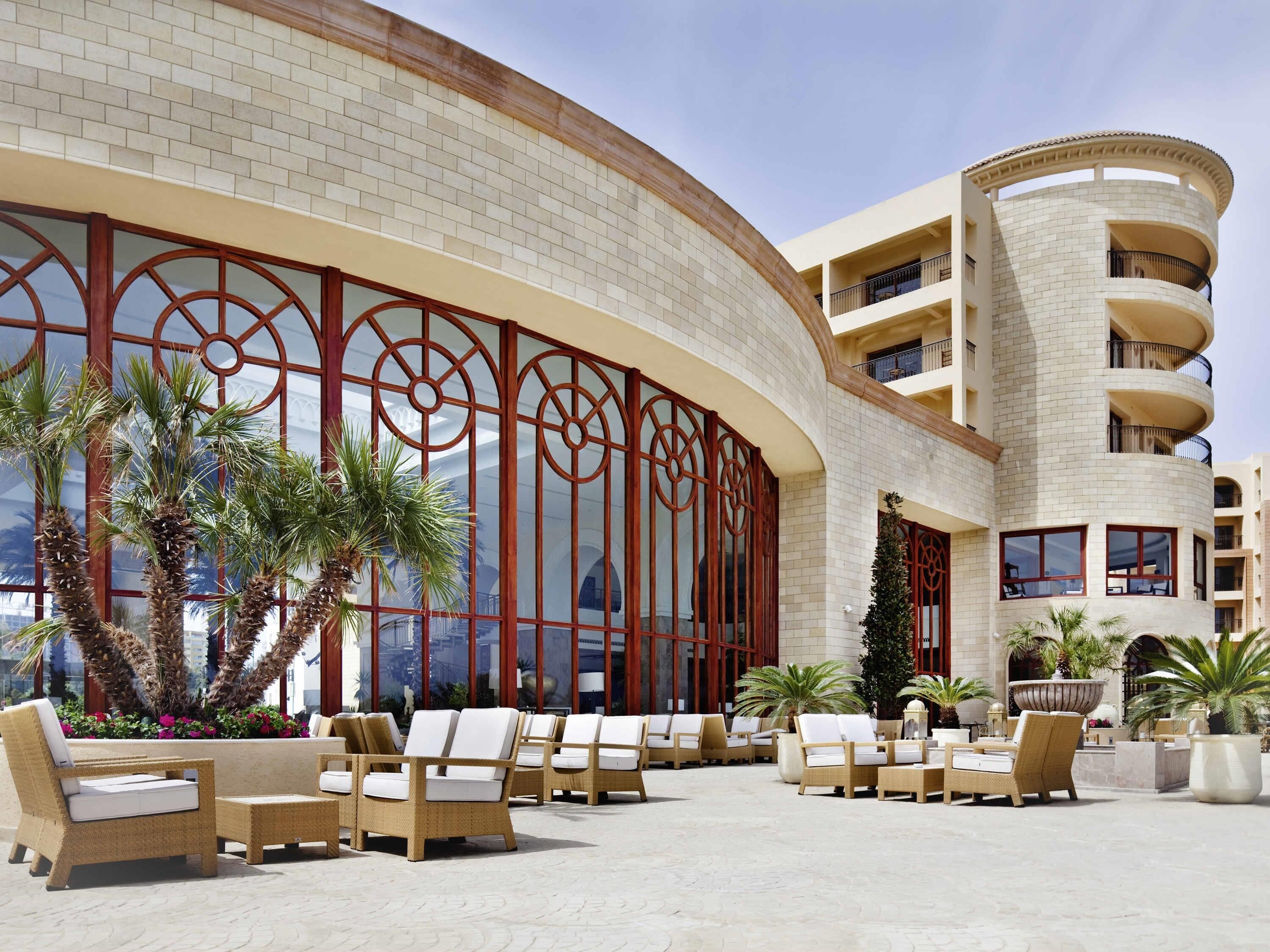 Un hotel con fachada curva, zona de estar al aire libre y palmeras.