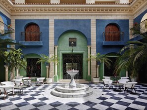 Un patio con una fuente, piso de tablones y mobiliario de mimbre blanco.