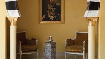 Una stanza con due poltrone decorate, un tavolino con un servizio da tè e un ritratto incorniciato appeso al muro.