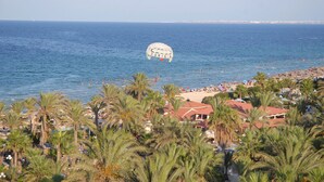 Una playa con palmeras y un paracaídas cuyo rótulo dice 'TUNISA' a lo lejos.