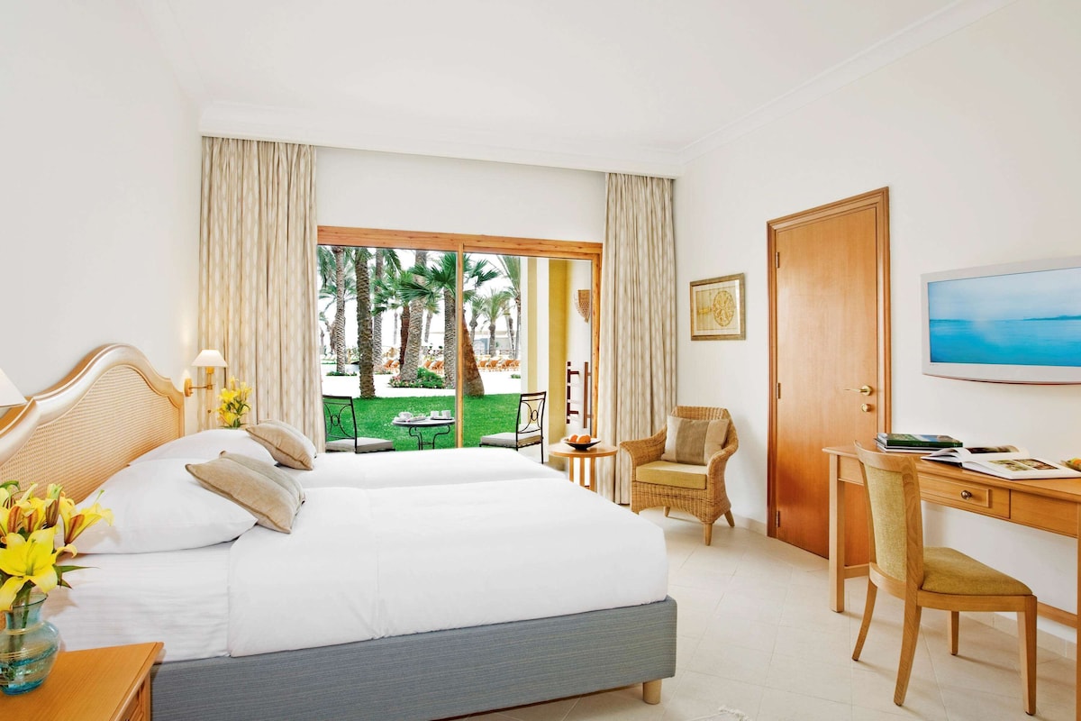 A hotel room with a large bed, a desk, a chair, and a television.