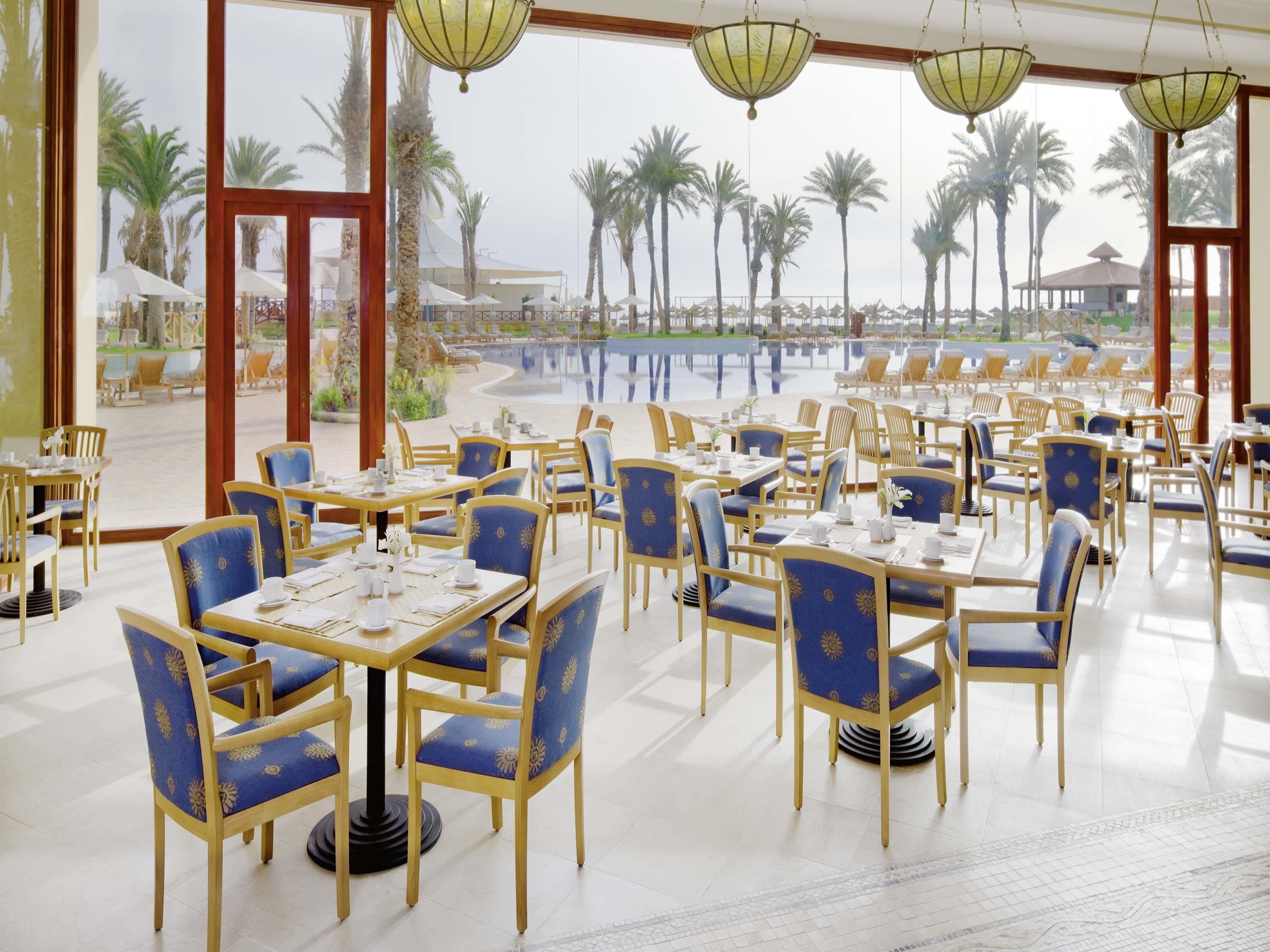 A restaurant with outdoor seating overlooking a pool and palm trees.