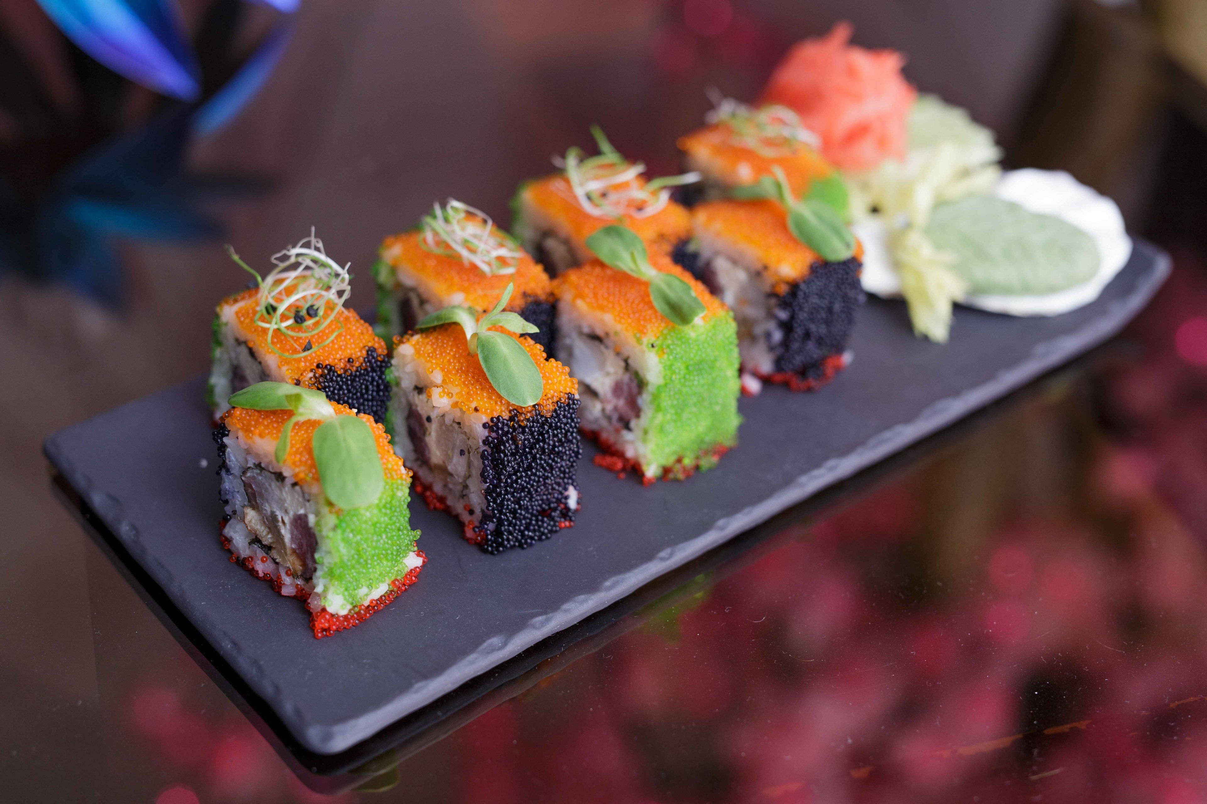 A black rectangular plate with sushi pieces, some with orange roe and green leaves, and a small salad with lettuce and a slice of tomato.