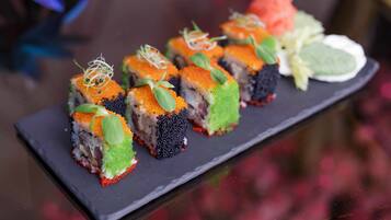 A black rectangular plate with sushi pieces, some with orange roe and green leaves, and a small salad with lettuce and a slice of tomato.