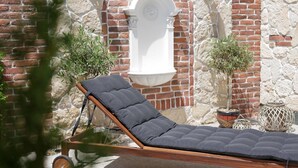 A sun lounger with a cushioned seat and wooden frame, positioned against a stone wall with a white column and decorative lanterns. - Weekend Boutique Hotel (Chisinau)