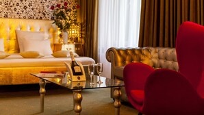 A luxurious bedroom with a bed, a glass coffee table with champagne, and a red armchair. - Weekend Boutique Hotel (Chisinau)