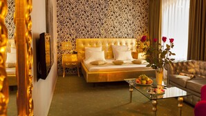 A luxurious living room with a gold-toned sofa, a tufted bed with white pillows, a glass coffee table with fruits, and a vase with flowers. - Weekend Boutique Hotel (Chisinau)