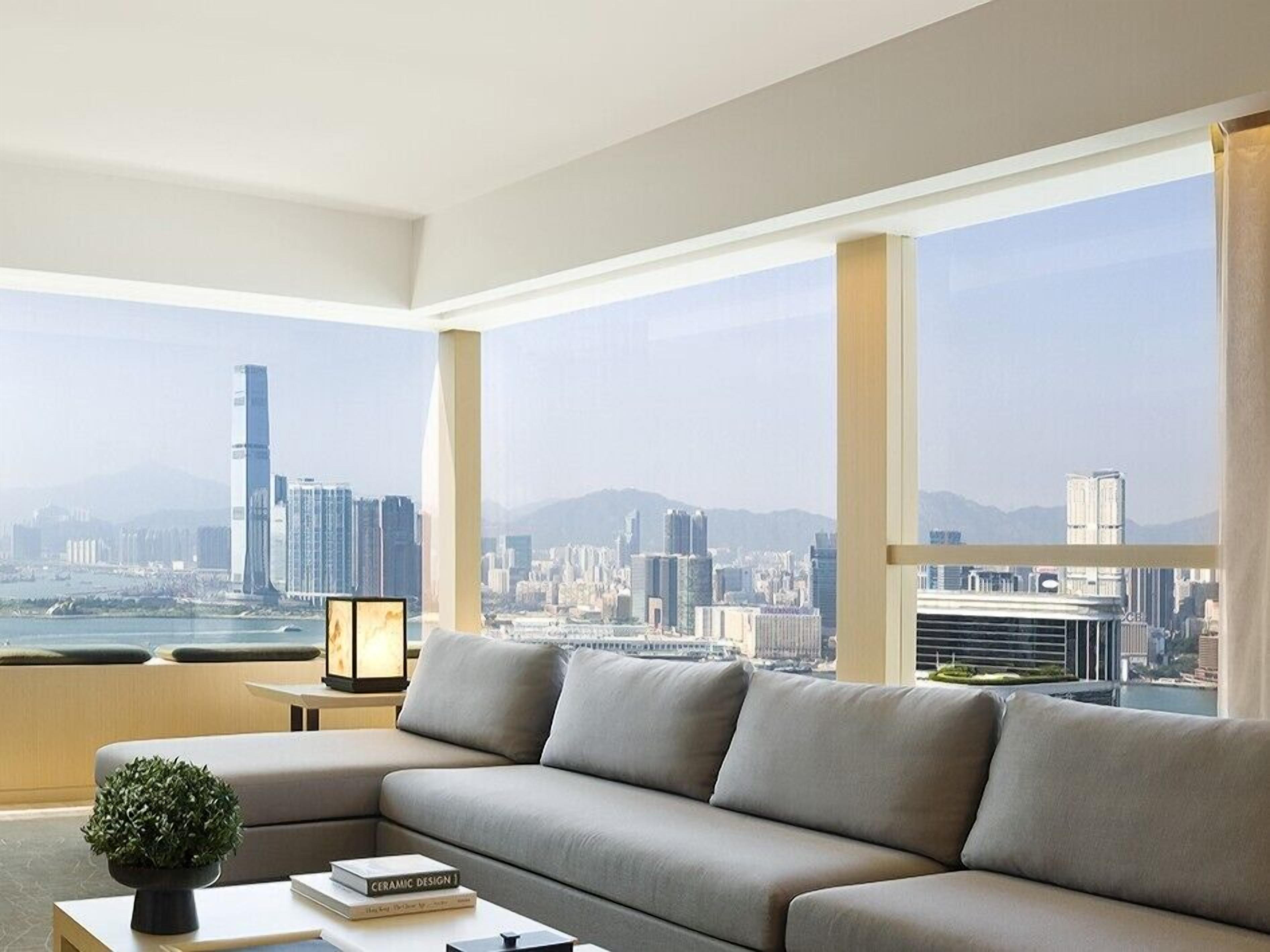 A modern living room with a sofa, a coffee table, and a view of a cityscape through large windows.