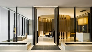 Un hall d’entrée moderne avec une cloison en verre, un comptoir d’accueil, un escalier et un mur décoratif en bois.