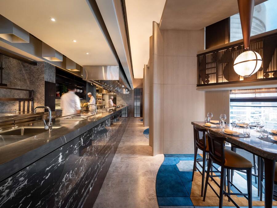 A modern kitchen with a long counter, stainless steel appliances, and a high ceiling.