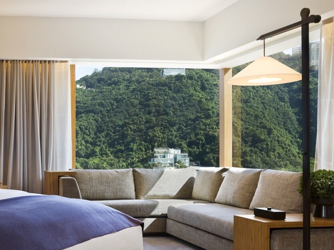 Une chambre d’hôtel moderne avec une grande fenêtre, un canapé, une table de chevet et une lampe.