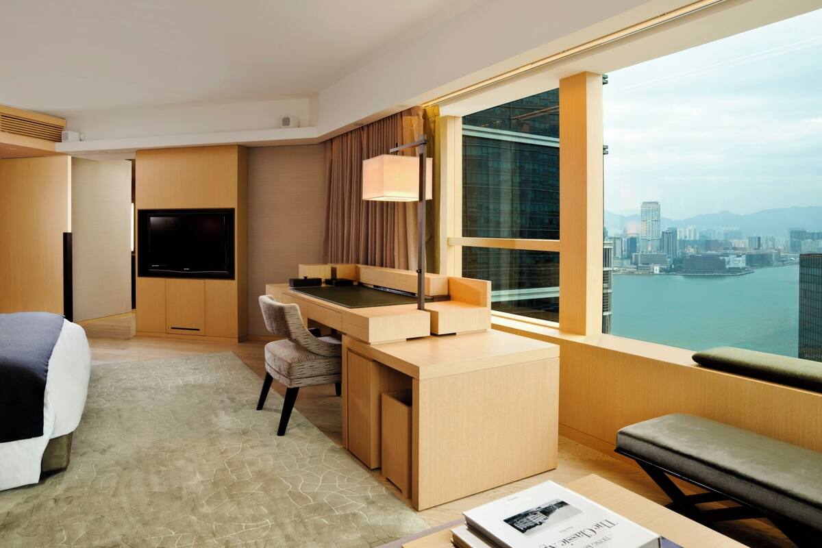 A modern hotel room with a large bed, a desk, a chair, a TV, and a view of the city and water.