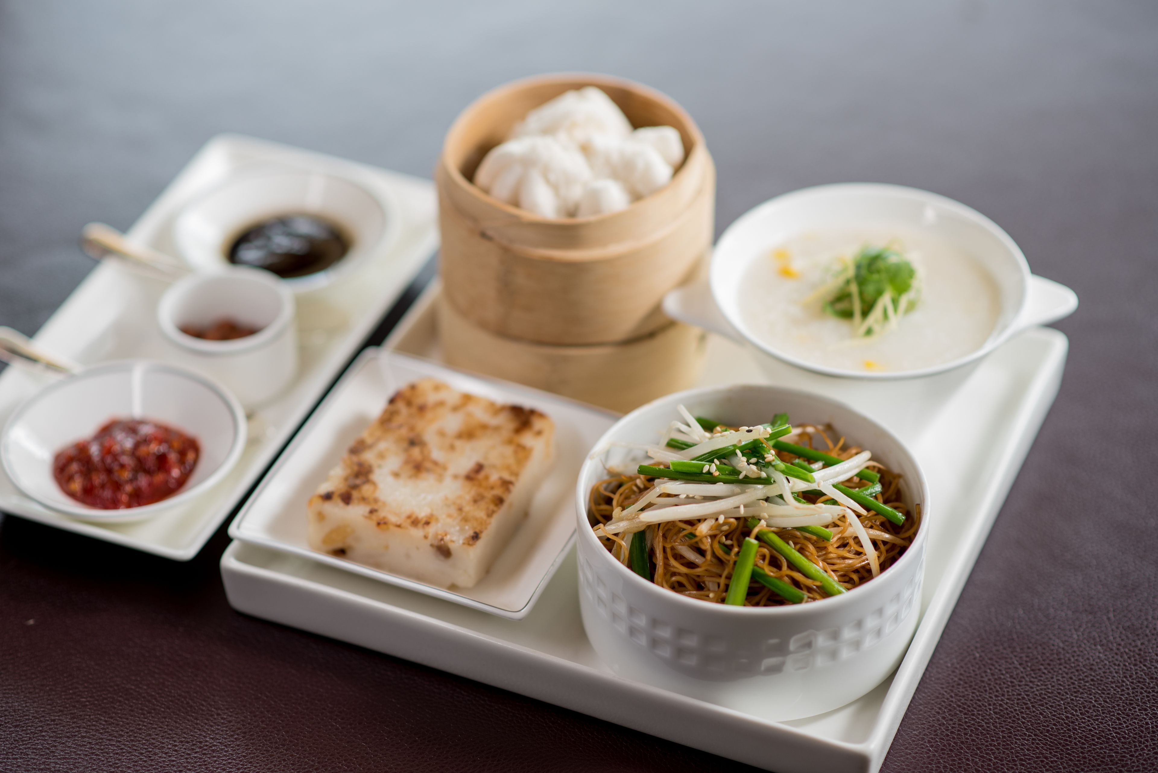 A tray with various dishes including a bowl of noodles, a piece of tofu, and a bowl of soup.
