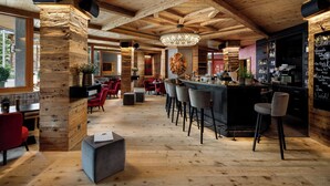Um espaço amplo de bar com vigas de madeira, um lustre e um balcão com banquetas.