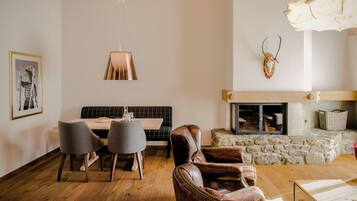 A dining area with a table, chairs, and a bench. There is a fireplace with a stone surround and a mounted deer skull.