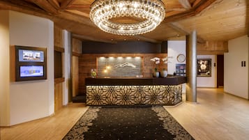 Un espace d’accueil doté d’un plafond en bois, d’un lustre, d’un comptoir de réception, d’un téléviseur fixé au mur et d’un tapis à motifs.