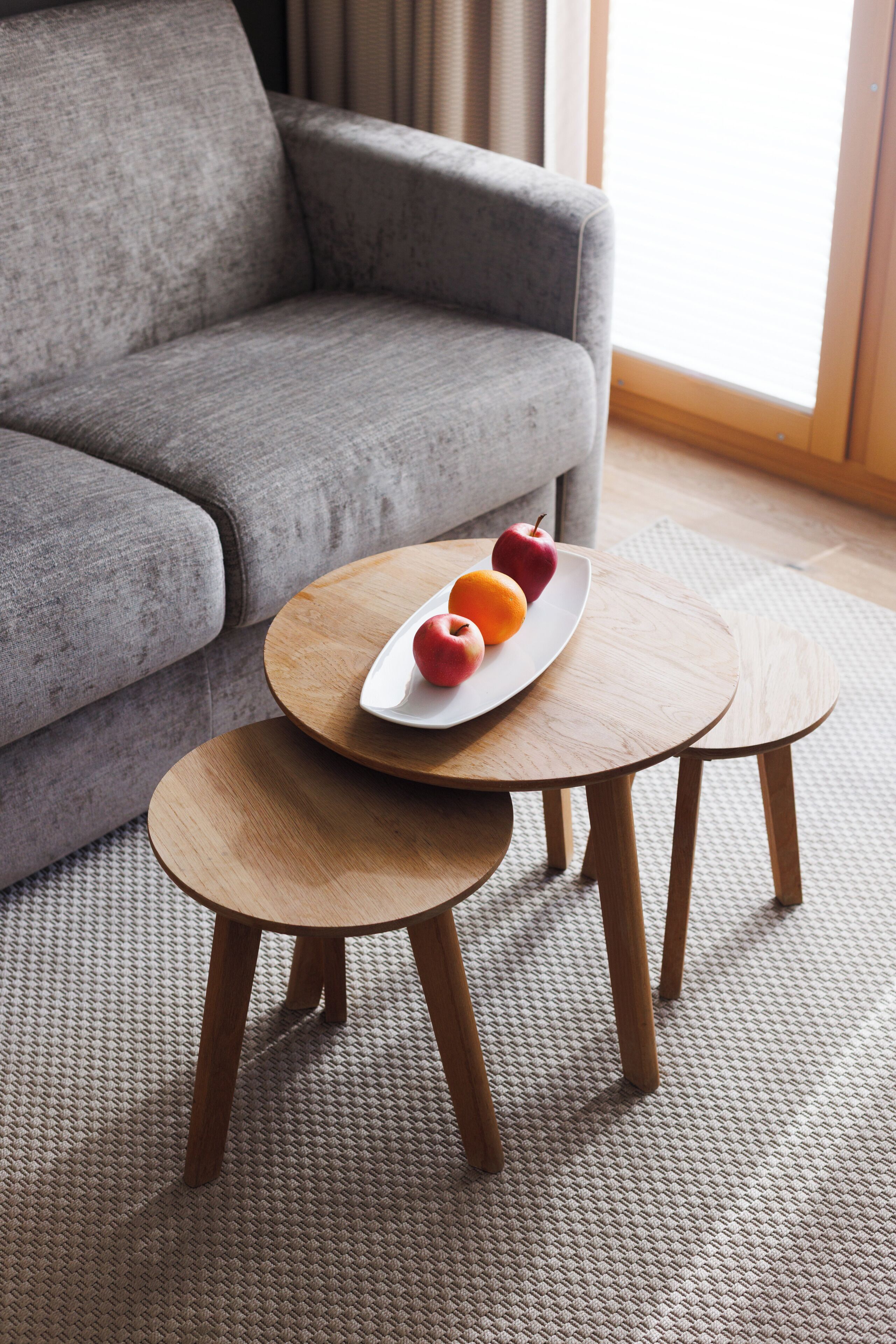 Un canapé gris, une petite table en bois sur laquelle se trouve une assiette de fruits, et un tabouret assorti.