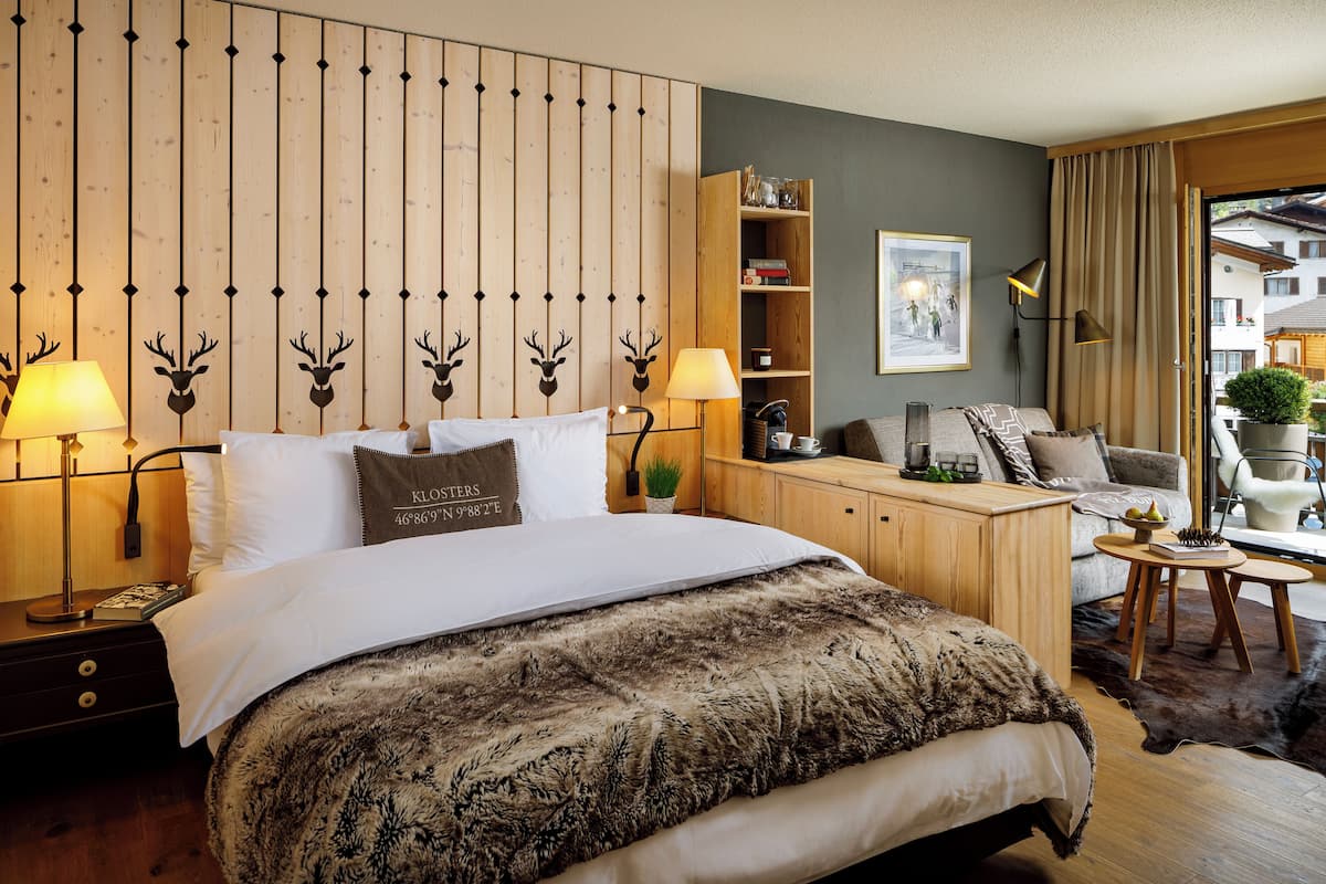 Habitación de hotel con cabecera de madera, una cama grande con una manta de piel, escritorio de madera, una silla y vistas al exterior.