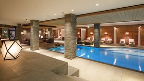 Piscina interior moderna com espreguiçadeiras e luminária geométrica.