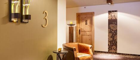 A hallway with a wooden door, a reception desk, and a chair.