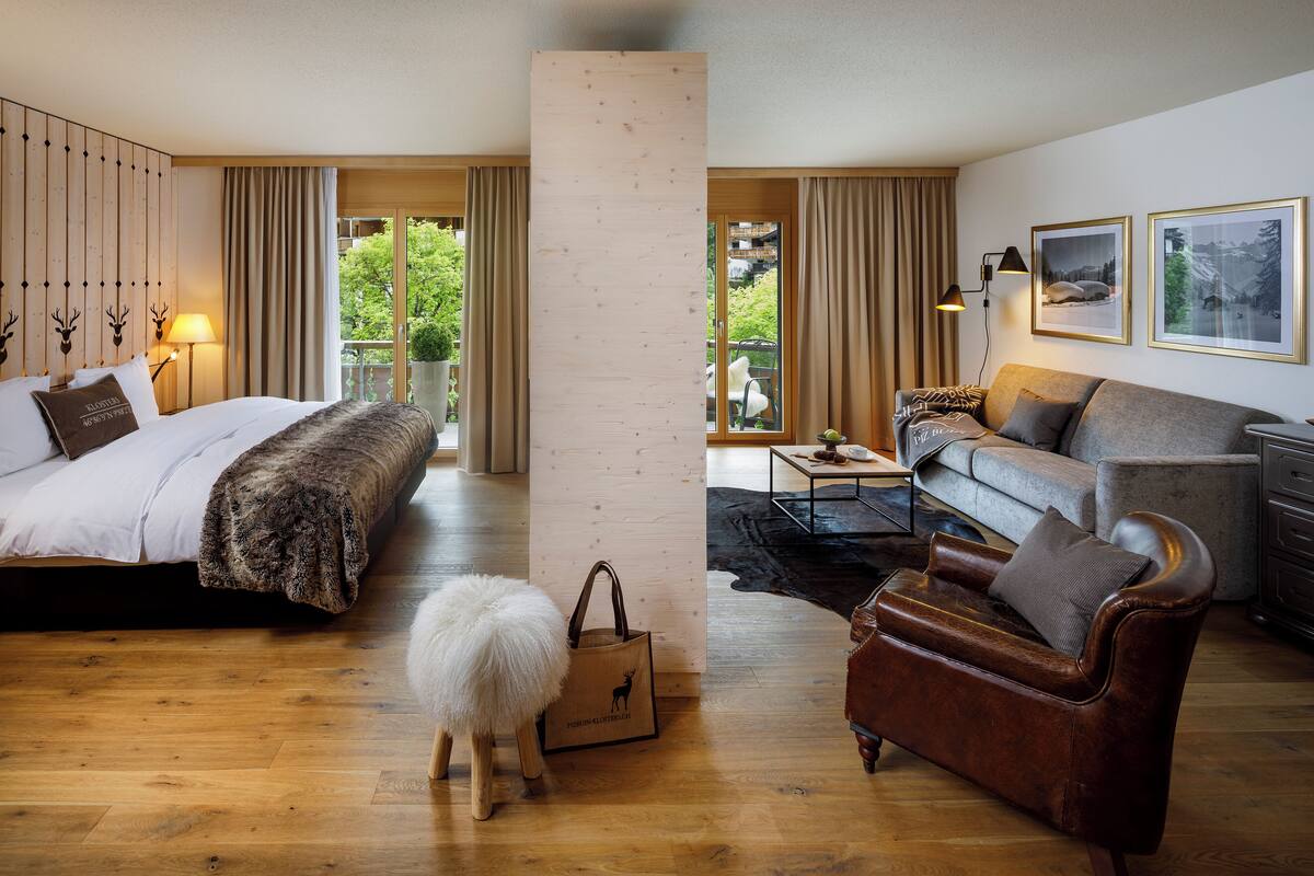 Habitación de hotel con cama, sofá, una mesita y vistas al verdor exterior.