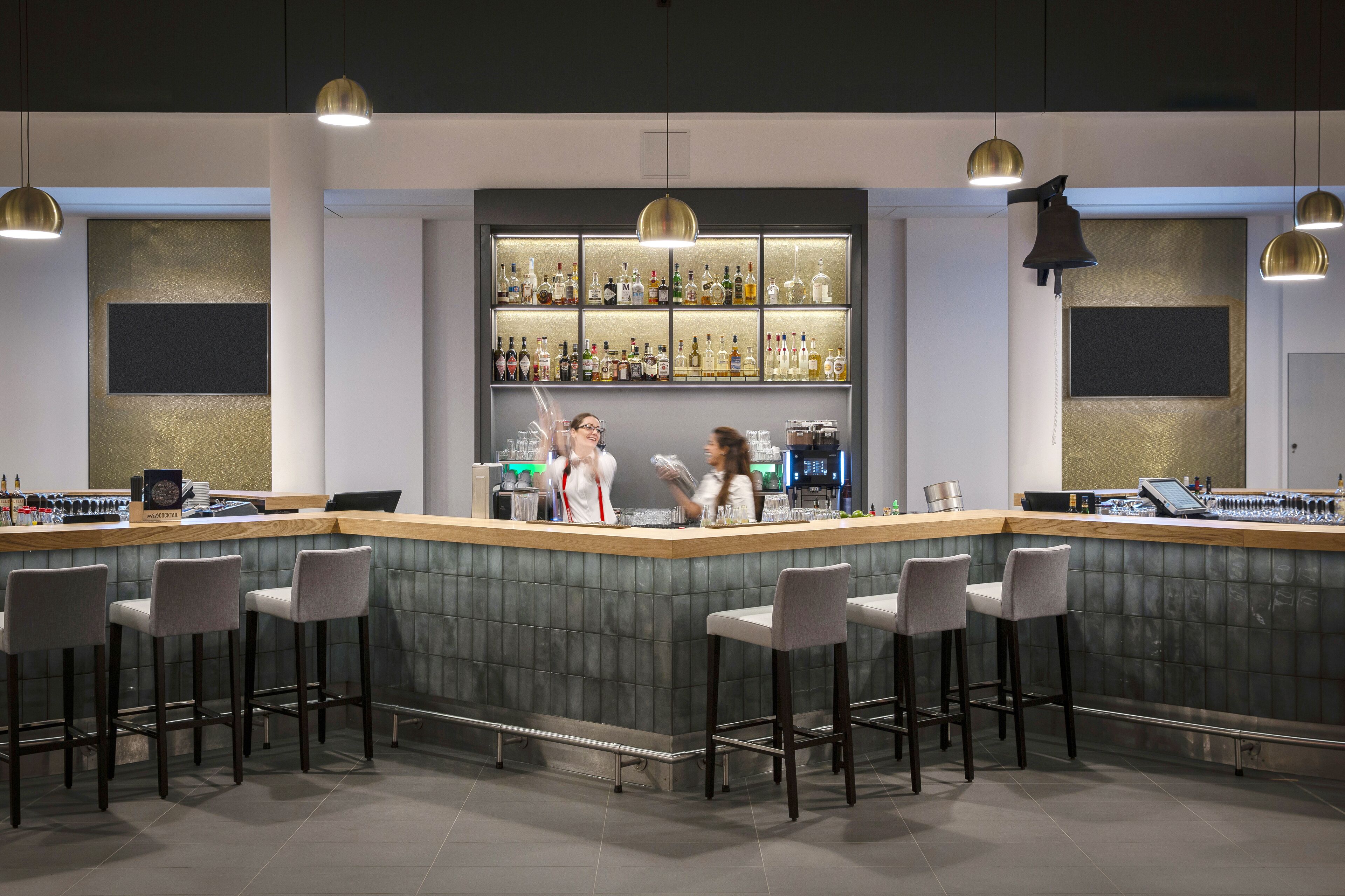A modern bar area with a bar counter, stools, and a well-stocked shelf of liquor bottles.