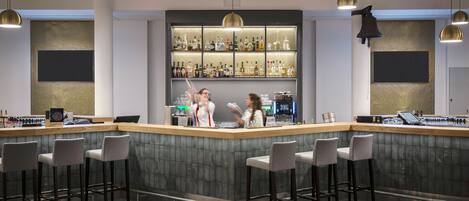 A modern bar area with a bar counter, stools, and a well-stocked shelf of liquor bottles.