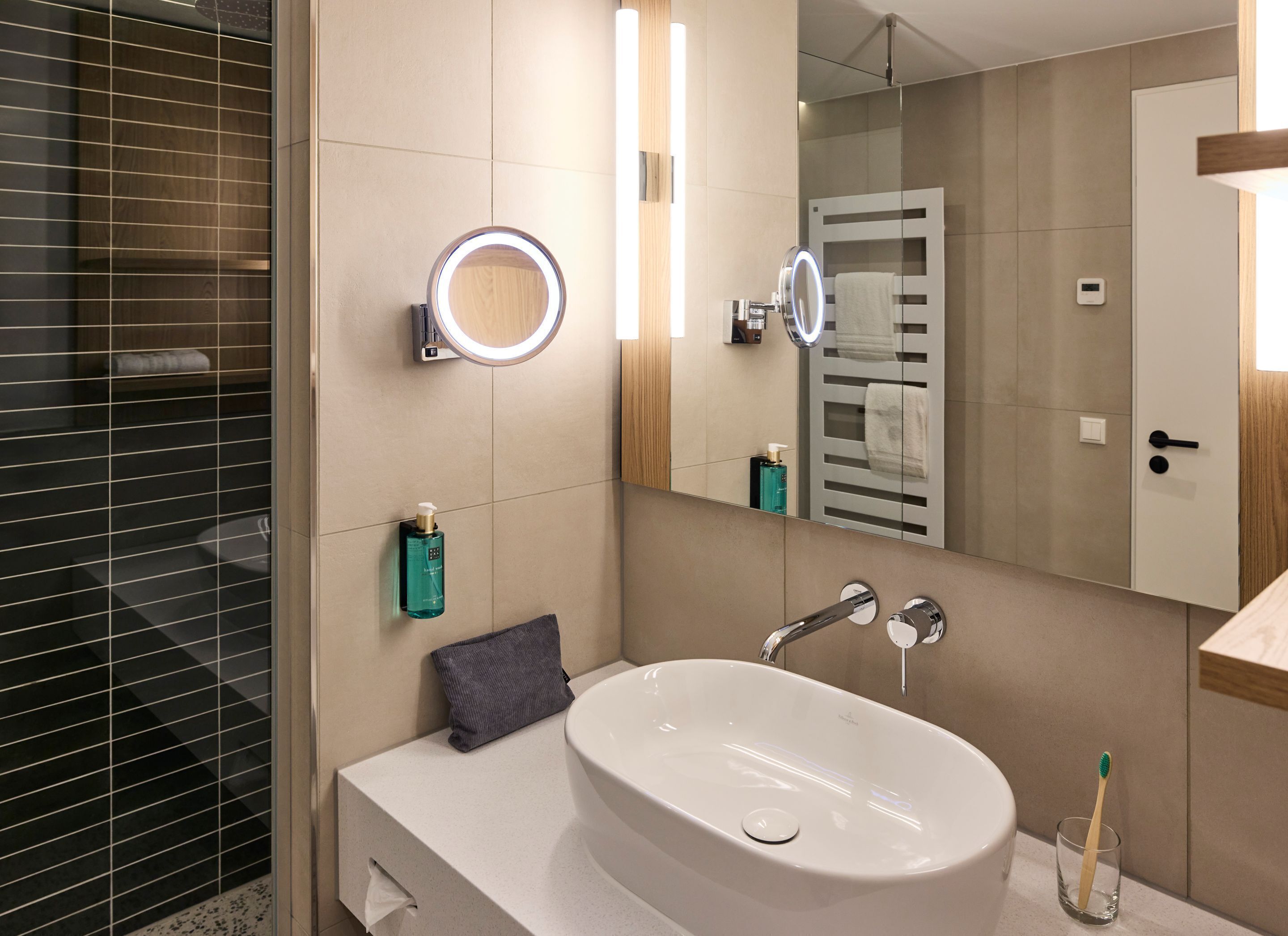 A modern bathroom with a large oval sink, a mirror with a ring light, a towel rack, and a glass of a toothbrush.
