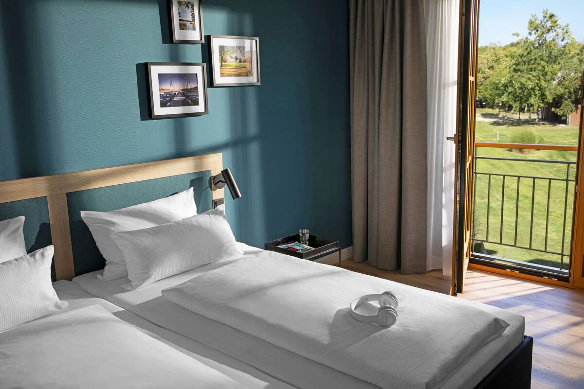 A hotel room with a large bed, a nightstand, and a view of a green lawn through an open door.