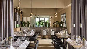 Un restaurant avec des tables dressées pour le service, des luminaires suspendus et une vue sur la verdure environnante.