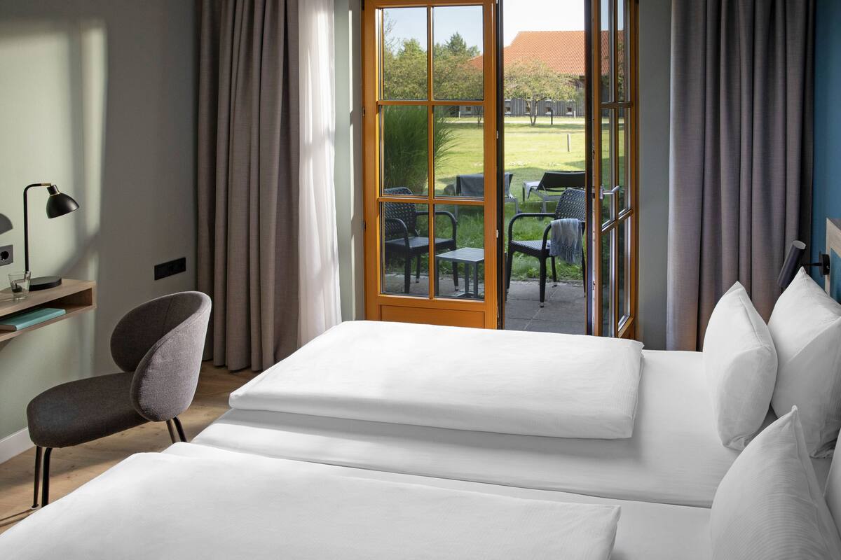 A hotel room with a large bed, a desk with a lamp, a chair, and a view of the outdoor patio area.