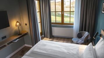 A bedroom with a bed, a chair, a TV, a window with curtains, and a lamp.