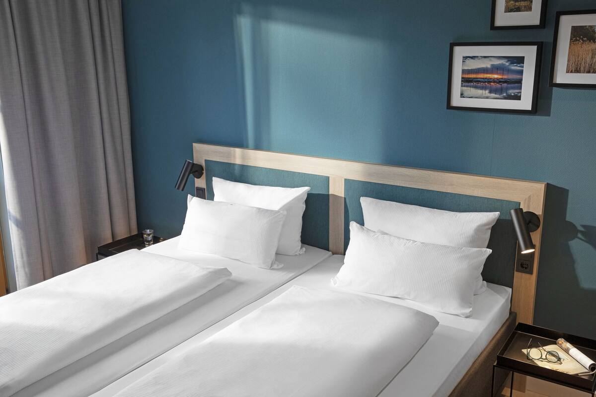 A double bed with white linens, a wooden headboard, and a nightstand with a lamp and a glass of water.