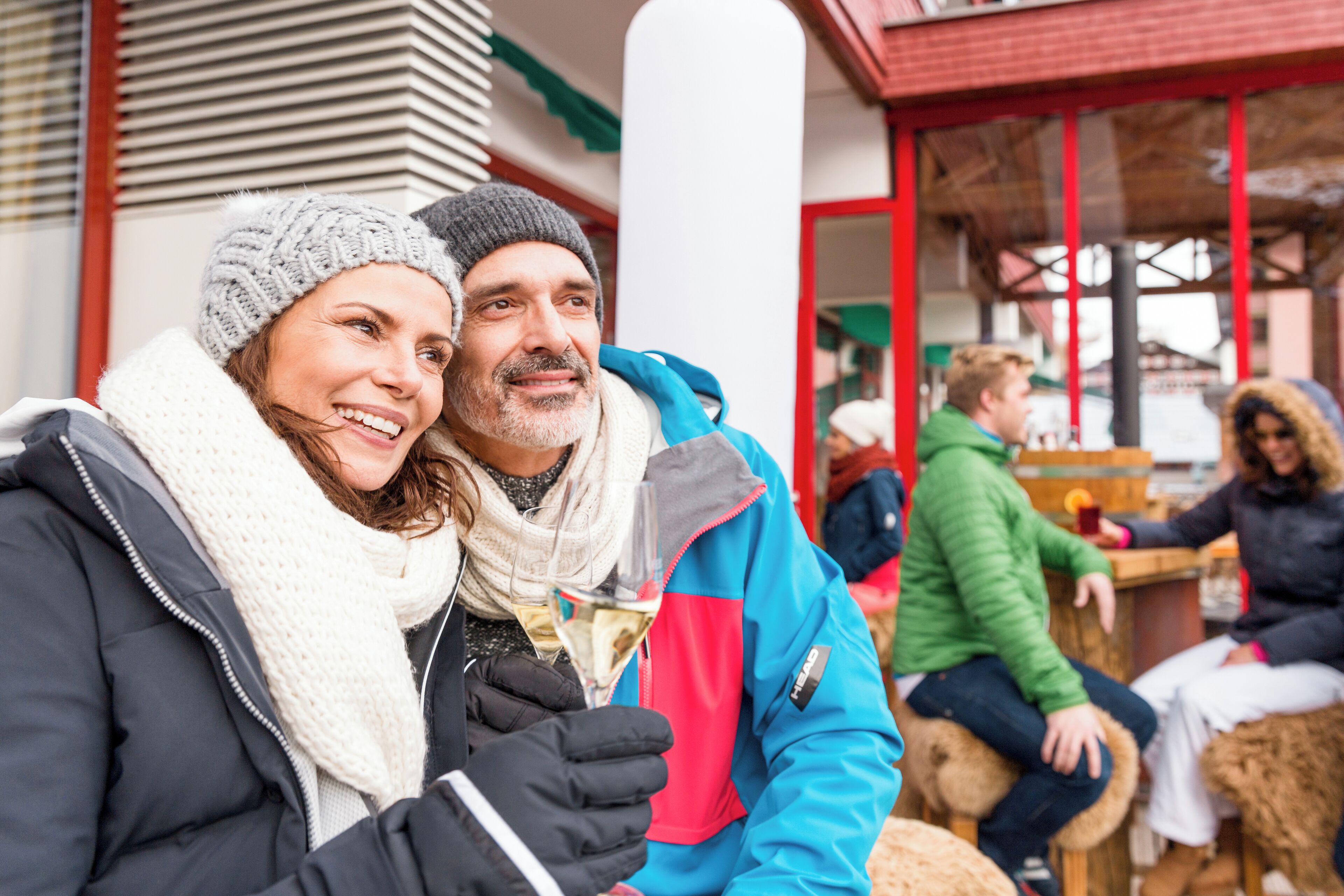 A couple embracing outdoors, with a building featuring red and white architecture in the background.